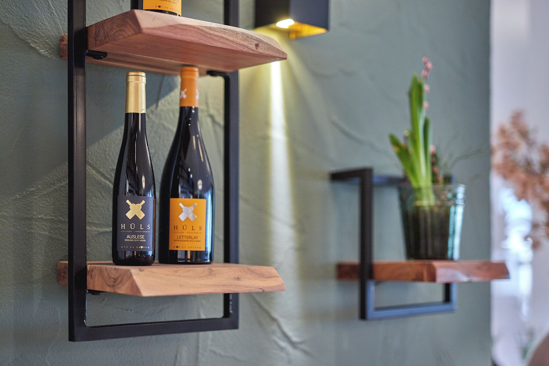Two wine bottles on a wooden shelf against a wall.