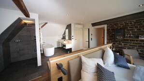 Un intérieur moderne avec une cheminée en pierre, un banc en bois, une baignoire blanche et un coin salon confortable agrémenté de coussins.