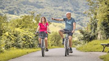 Duas pessoas de bicicleta em um caminho pavimentado, rodeadas por vegetação.
