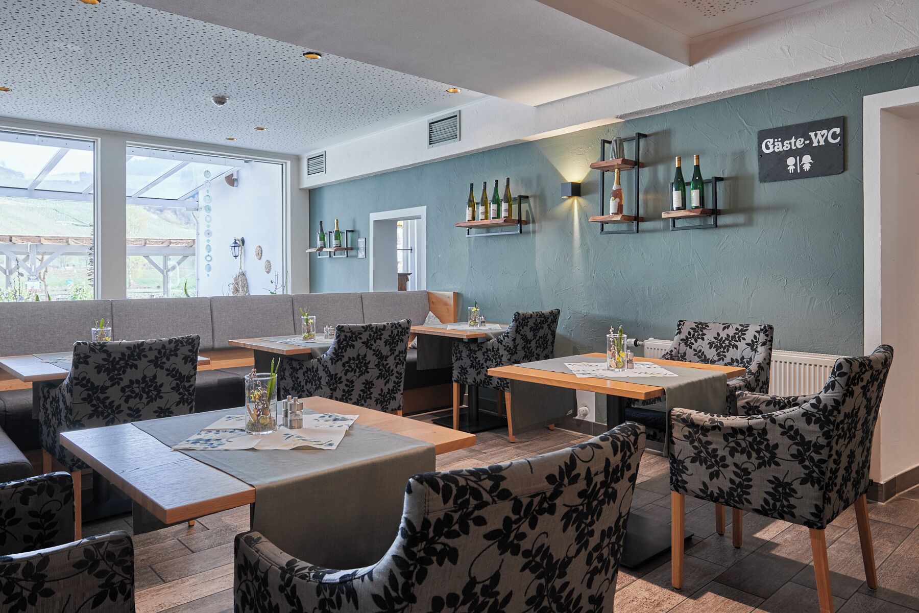 A restaurant interior with booths and tables, a wall-mounted wine rack, and a sign reading "Gäste-VIC".