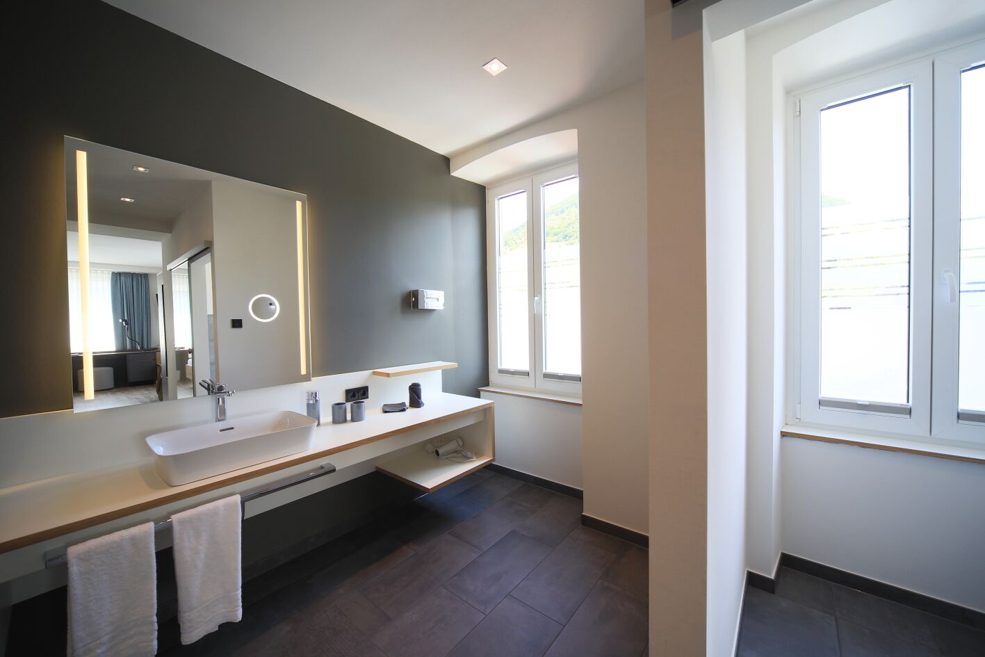 A modern bathroom with a large mirror, two sinks, and a window.