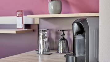Een koffieapparaat op een houten aanrecht, met een bloevas en een bord in de achtergrond.