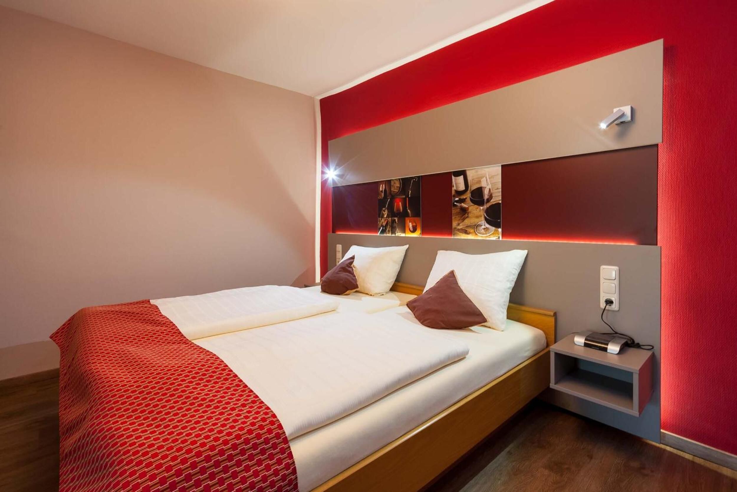 A hotel room with a bed, a nightstand, and a wall-mounted shelf with pictures.