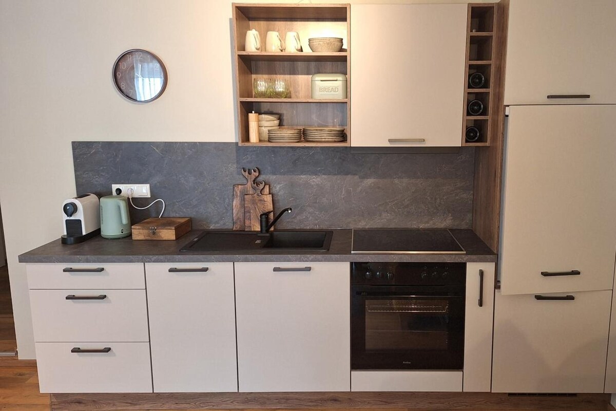 A modern kitchen with a built-in oven, a sink, and a countertop with a toaster and kettle.