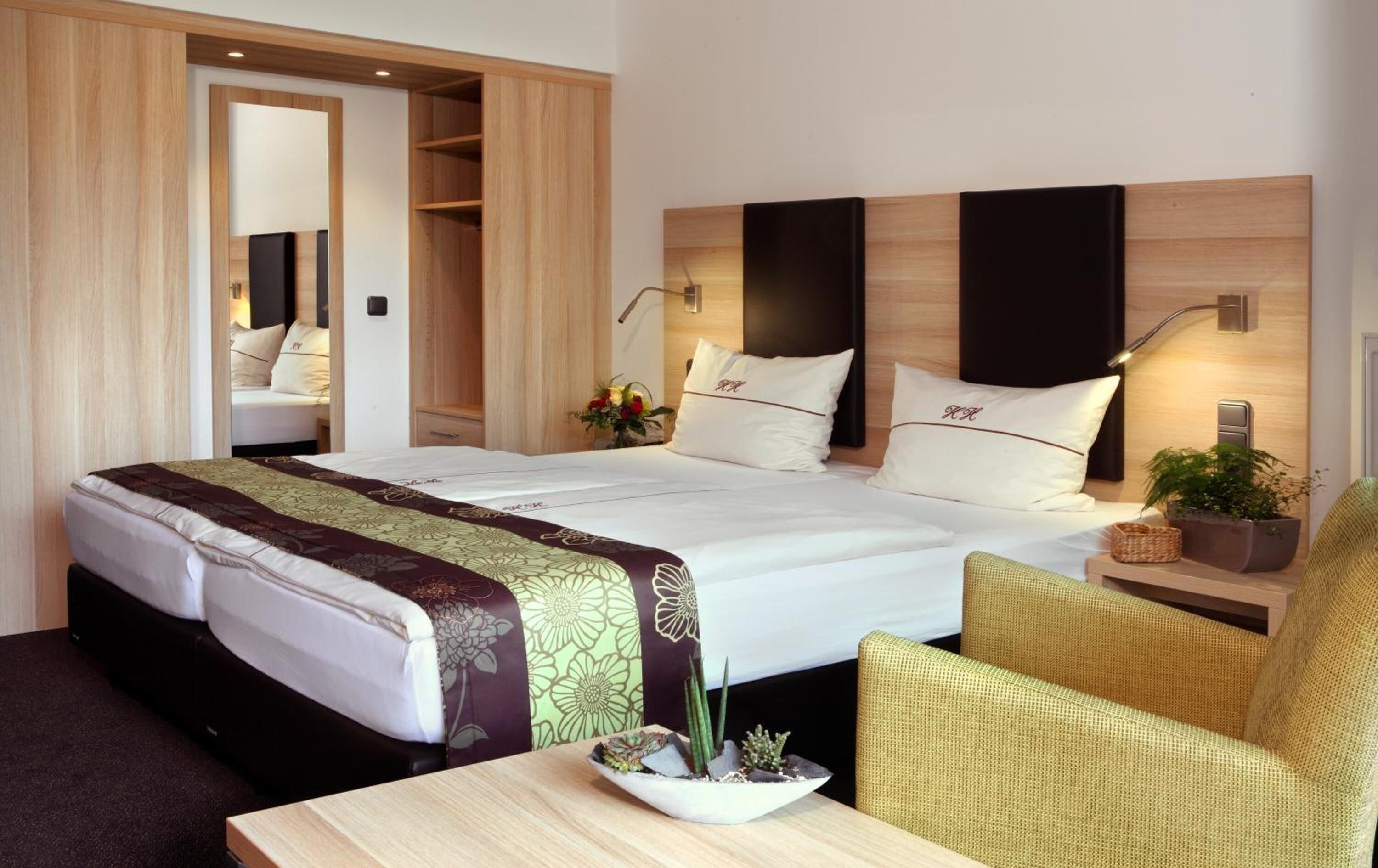 Una habitación de hotel con una cama grande, una mesita de noche con una planta, una silla y un armario.