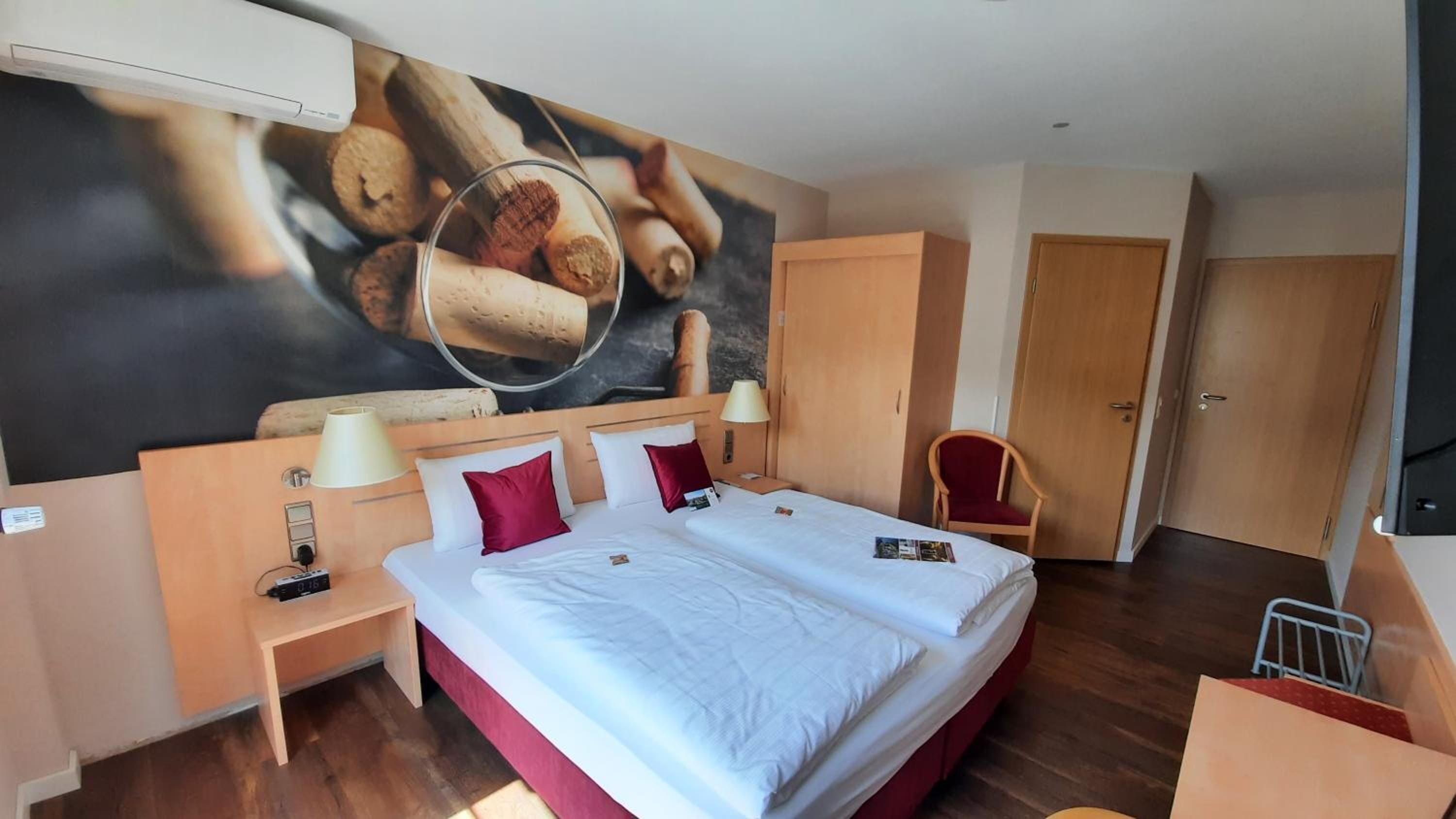 A hotel room with a large bed, two bedside tables, a desk, a chair, and a wall mural.