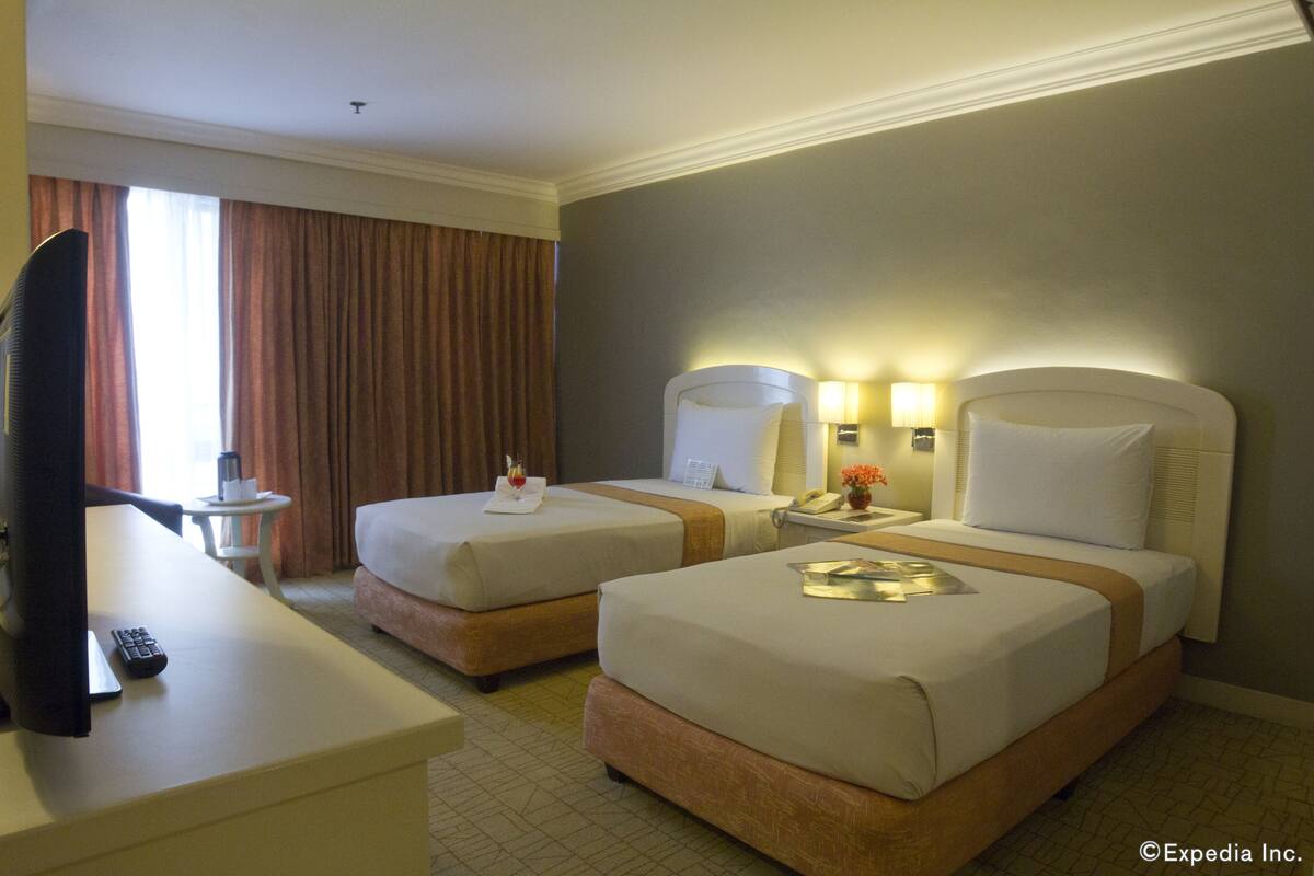 A hotel room with two beds, a TV, a desk, and a small table with a lamp.