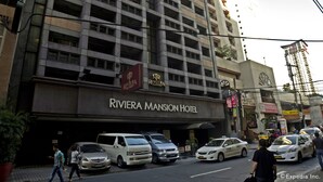 The exterior of the Riviera Mansion Hotel with multiple floors, a prominent entrance, and several parked cars in front. - Riviera Mansion Hotel (Manila)