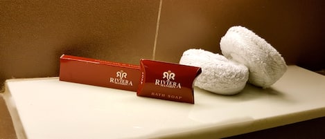 Dos jabones de baño Riviera Mansion y dos toallas blancas sobre un estante blanco.