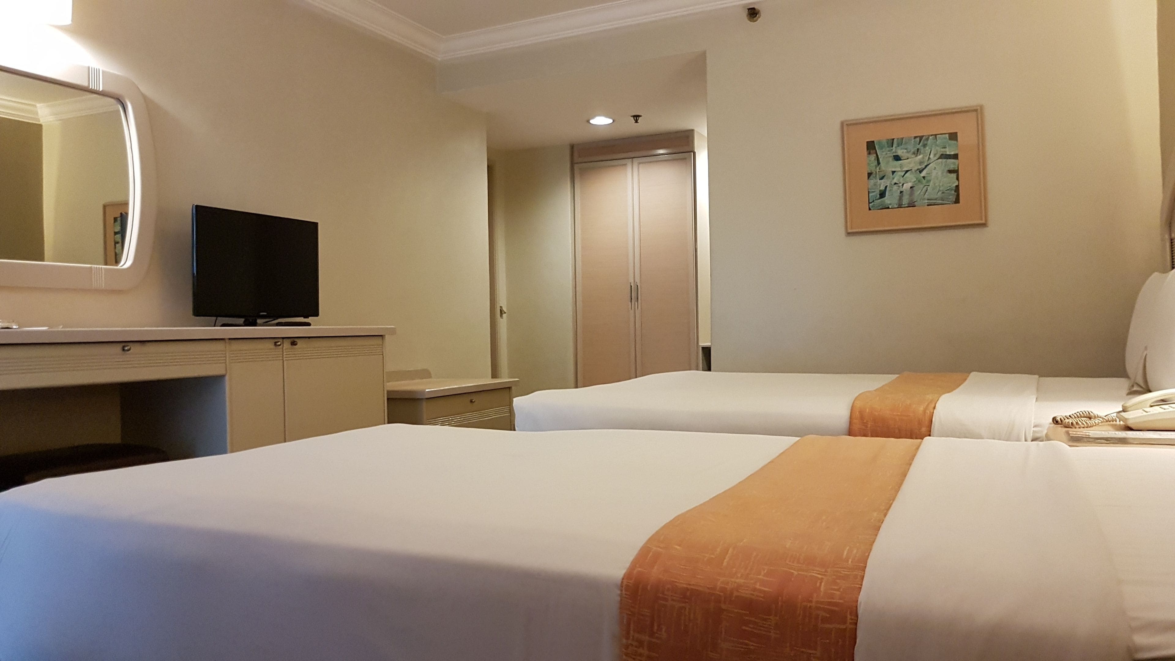 Habitación de hotel con dos camas, un escritorio con televisor, un armario y un cuadro en la pared.