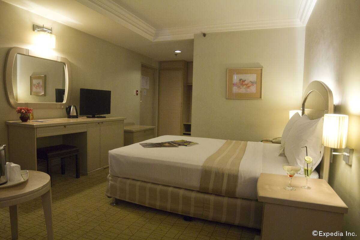 A hotel room with a bed, bedside table, lamp, and a desk with a television and computer.