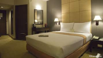 A hotel room with a large bed, bedside lamps, a nightstand with a phone, a dresser, and a mirror.