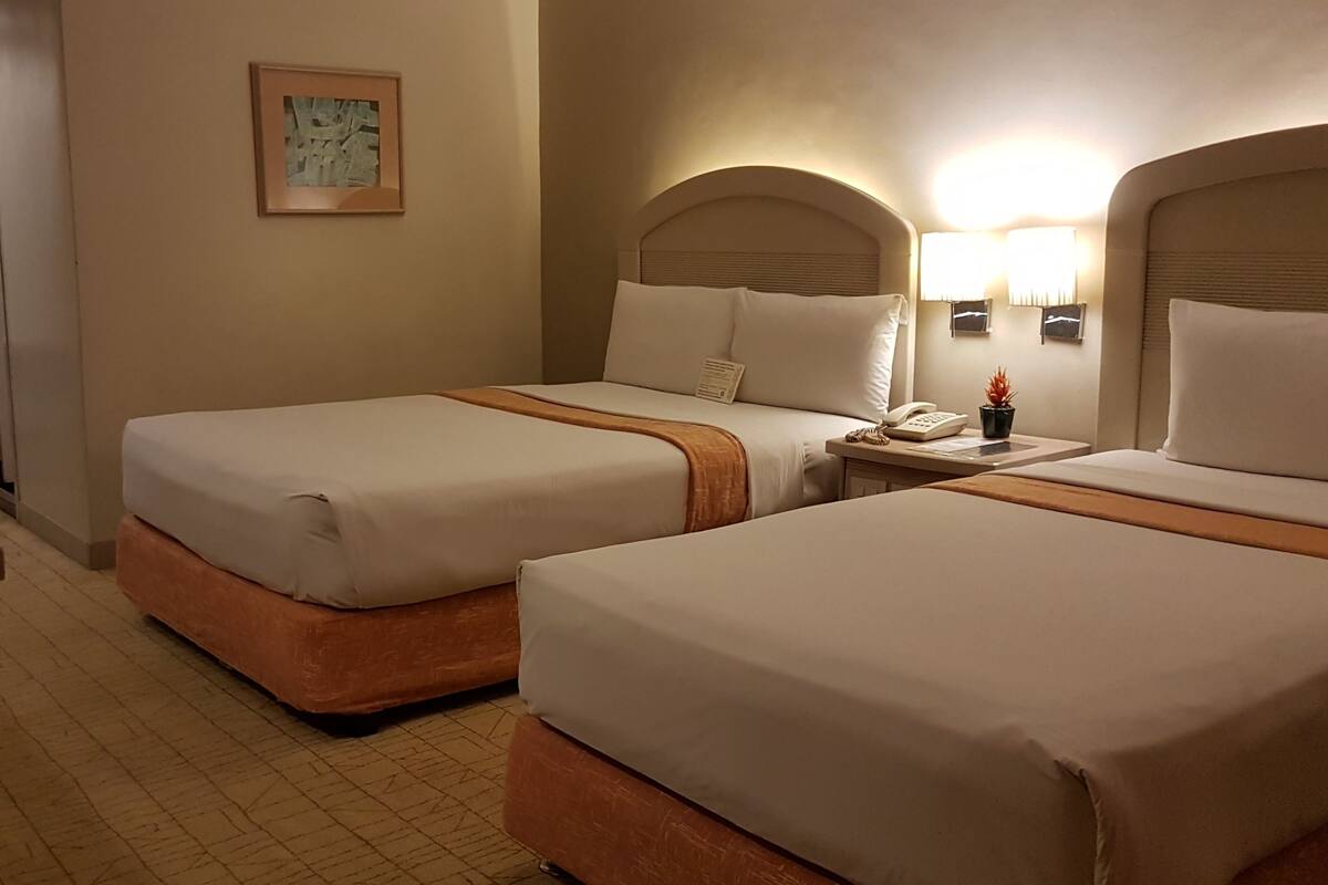 A hotel room with two beds, a desk, a chair, a phone, and a small plant.