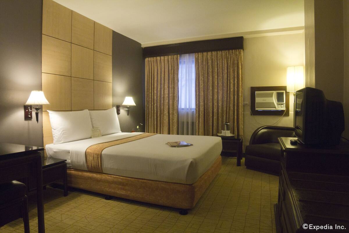 A hotel room with a large bed, two bedside lamps, a television, a desk, and a chair.
