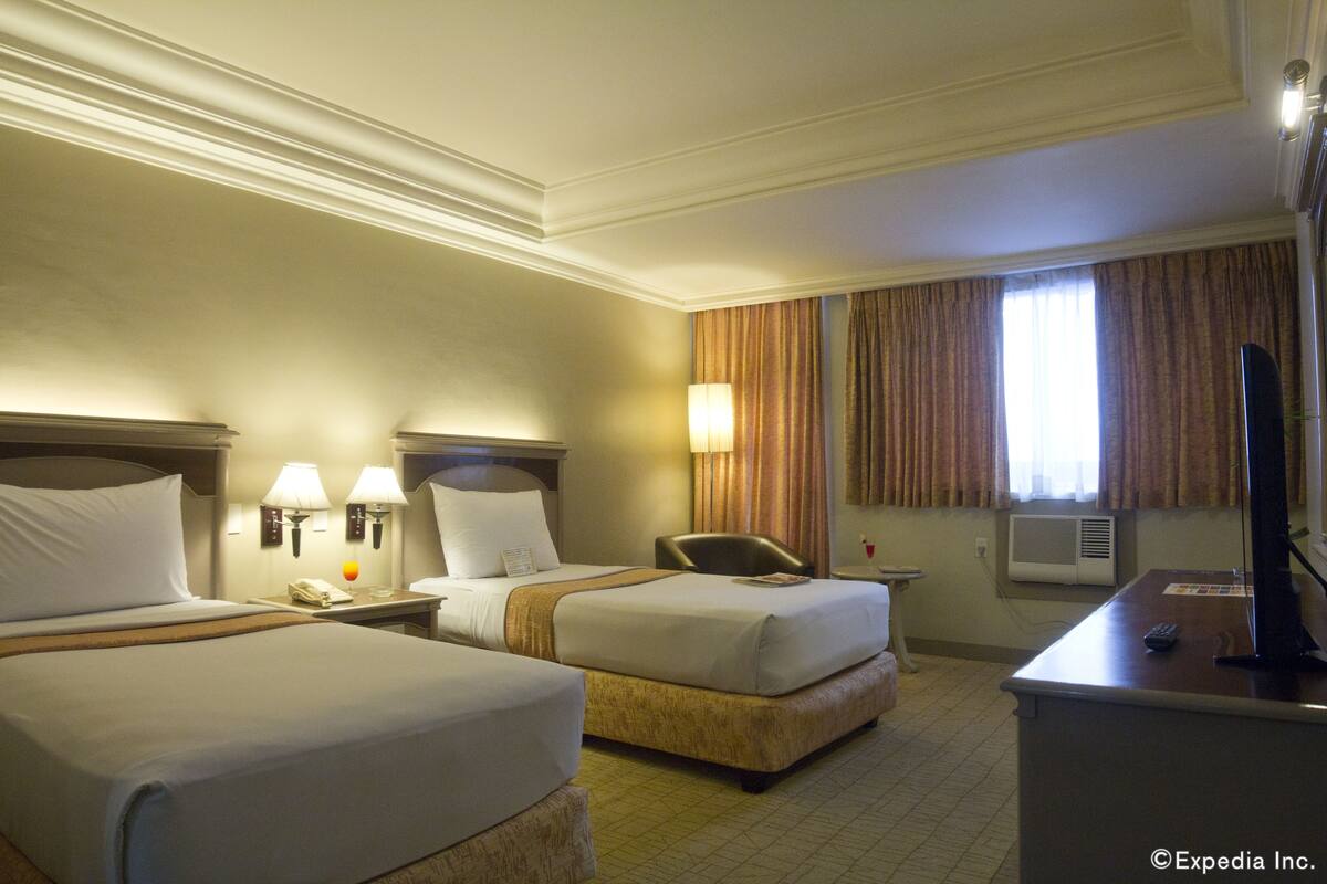 A hotel room with two beds, a desk with a computer, and a window with curtains.