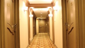 A hotel hallway with patterned carpet, wooden doors, and wall sconces. - Riviera Mansion Hotel (Manila)