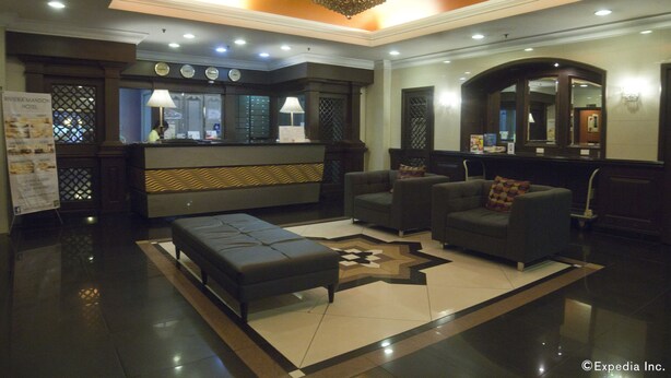 A lobby with a reception desk, seating area, and a large mirror. - Riviera Mansion Hotel (Manila)