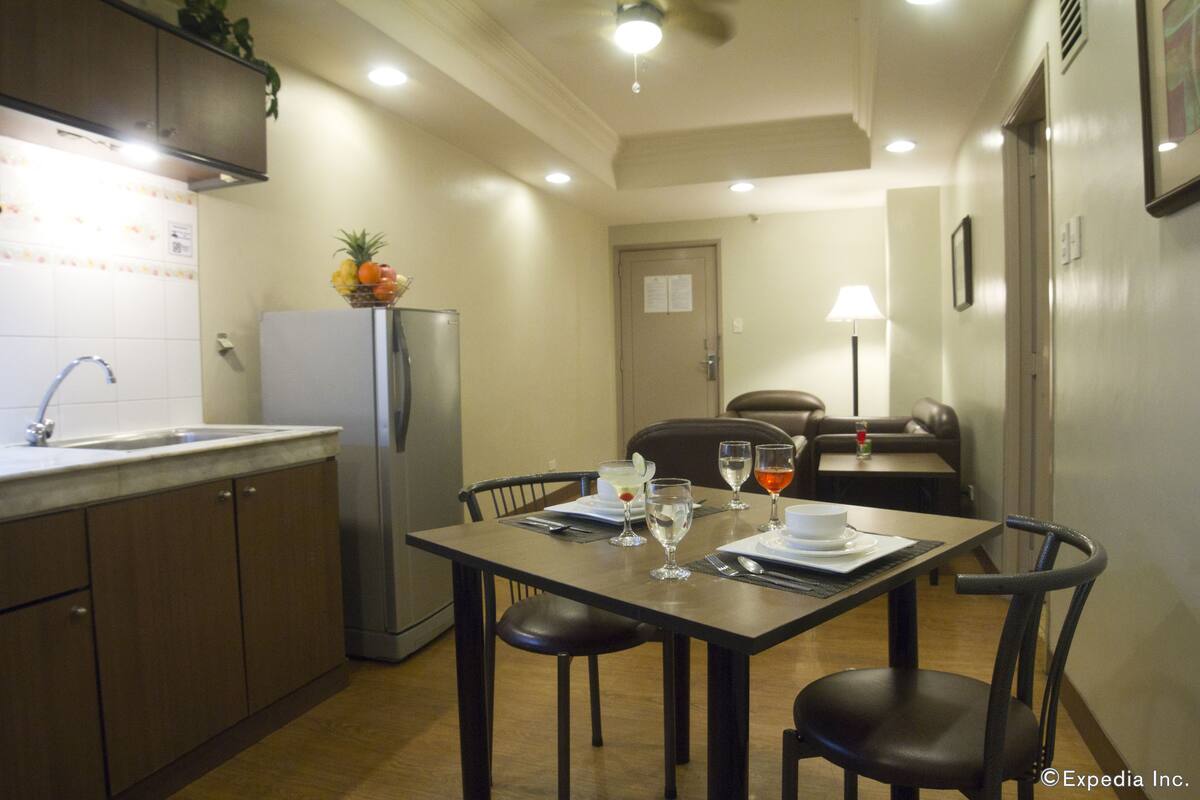 A compact kitchen with a refrigerator, sink, and a dining area with chairs and a table set for two.