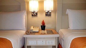 A hotel room with two beds, a bedside table with a phone, a lamp, and a potted plant.