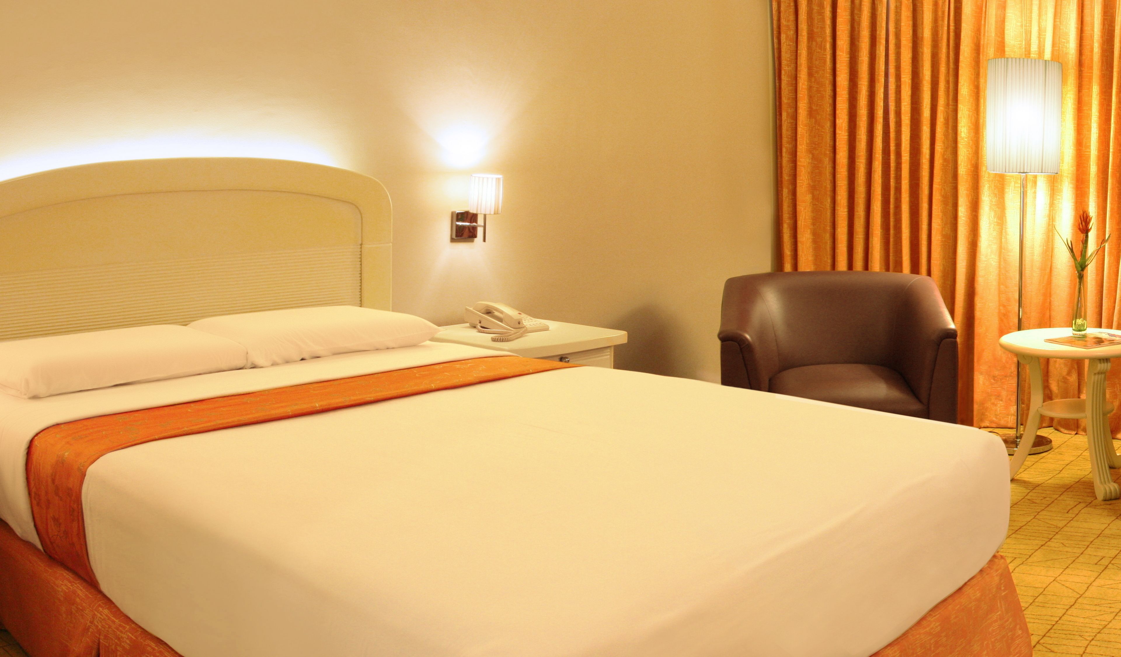 Una habitación de hotel con una cama grande, una mesita de noche con teléfono, una silla y una pequeña mesa con un florero.