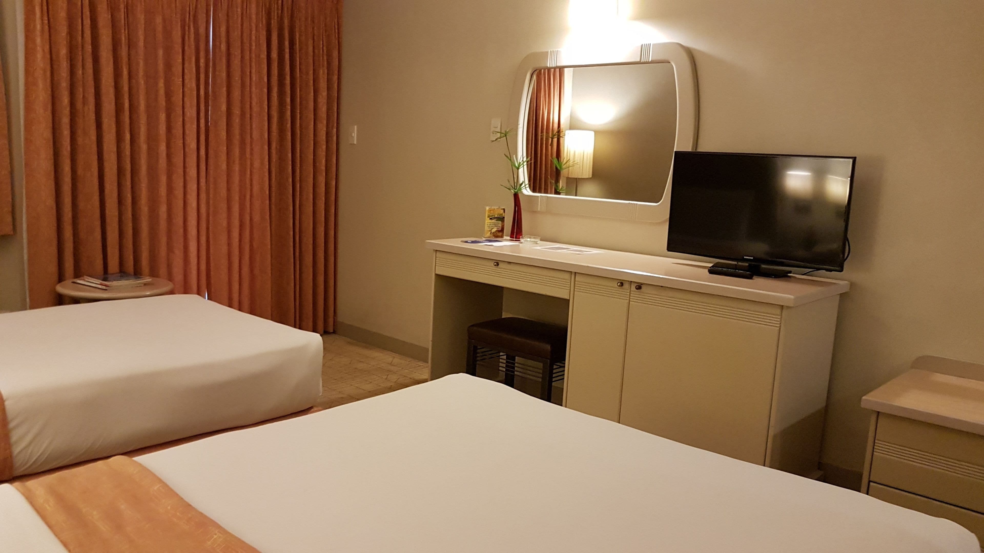 A hotel room with two beds, a desk with a television, a small table, and a chair.