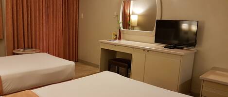 Habitación de hotel con dos camas, un escritorio con televisor, una mesita y una silla.