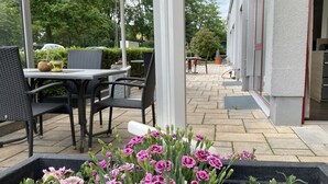 Un patio al aire libre con una mesa y sillas, una jardinera con flores y un edificio al fondo.