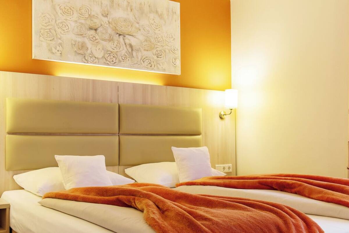 A hotel room with a large bed, two bedside lamps, a headboard, and a wall-mounted artwork.