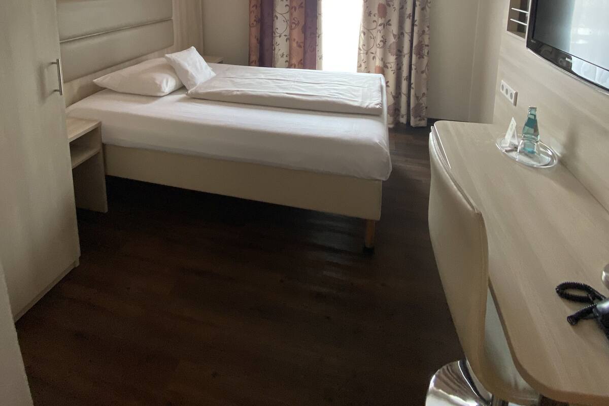 A hotel room with a bed, a desk, a television, and a wardrobe.
