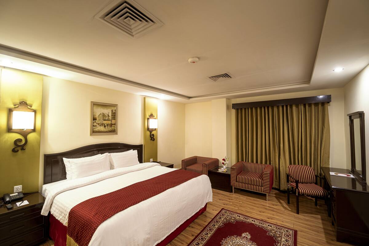 Een hotelkamer met een groot bed, twee fauteuils, een bureau en een spiegel.