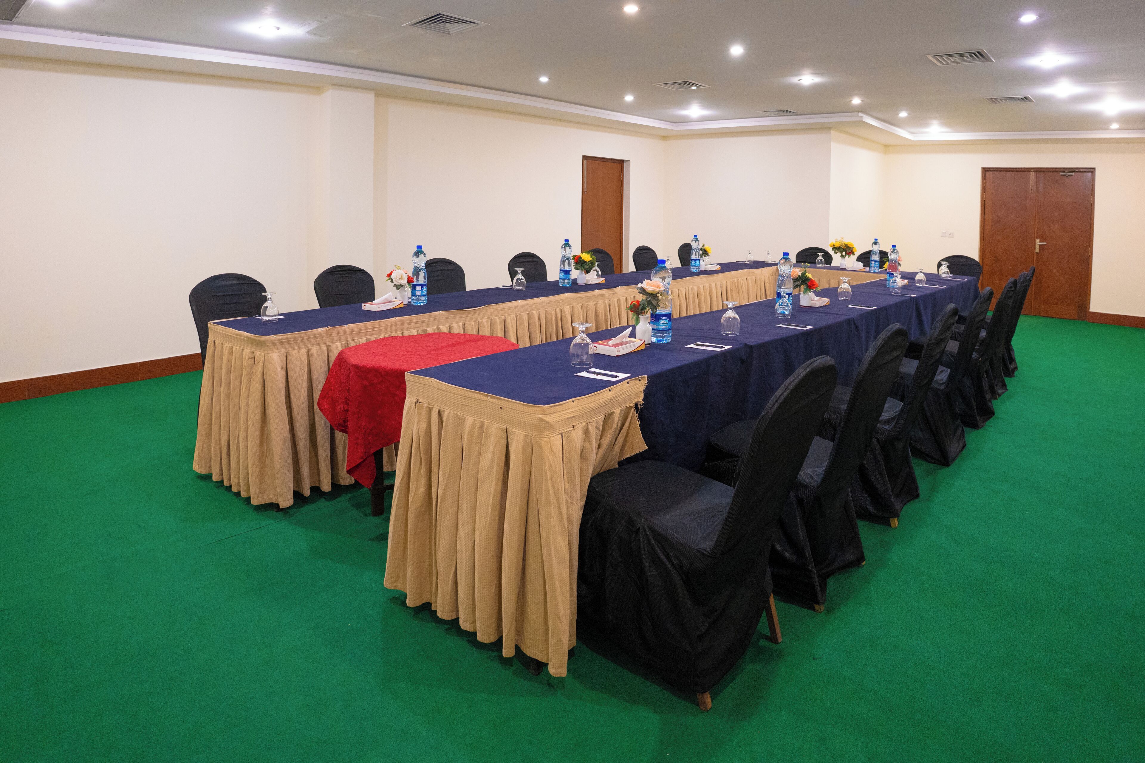 Un salón de conferencias con una mesa larga, sillas y botellas de agua.
