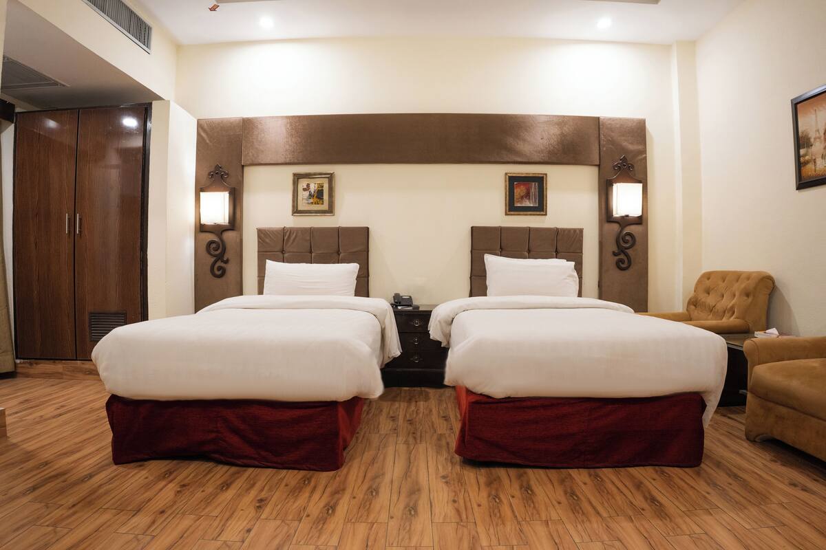 Een hotelkamer met twee bedden, houten vloeren, een grote kledingkast en wandlampen.