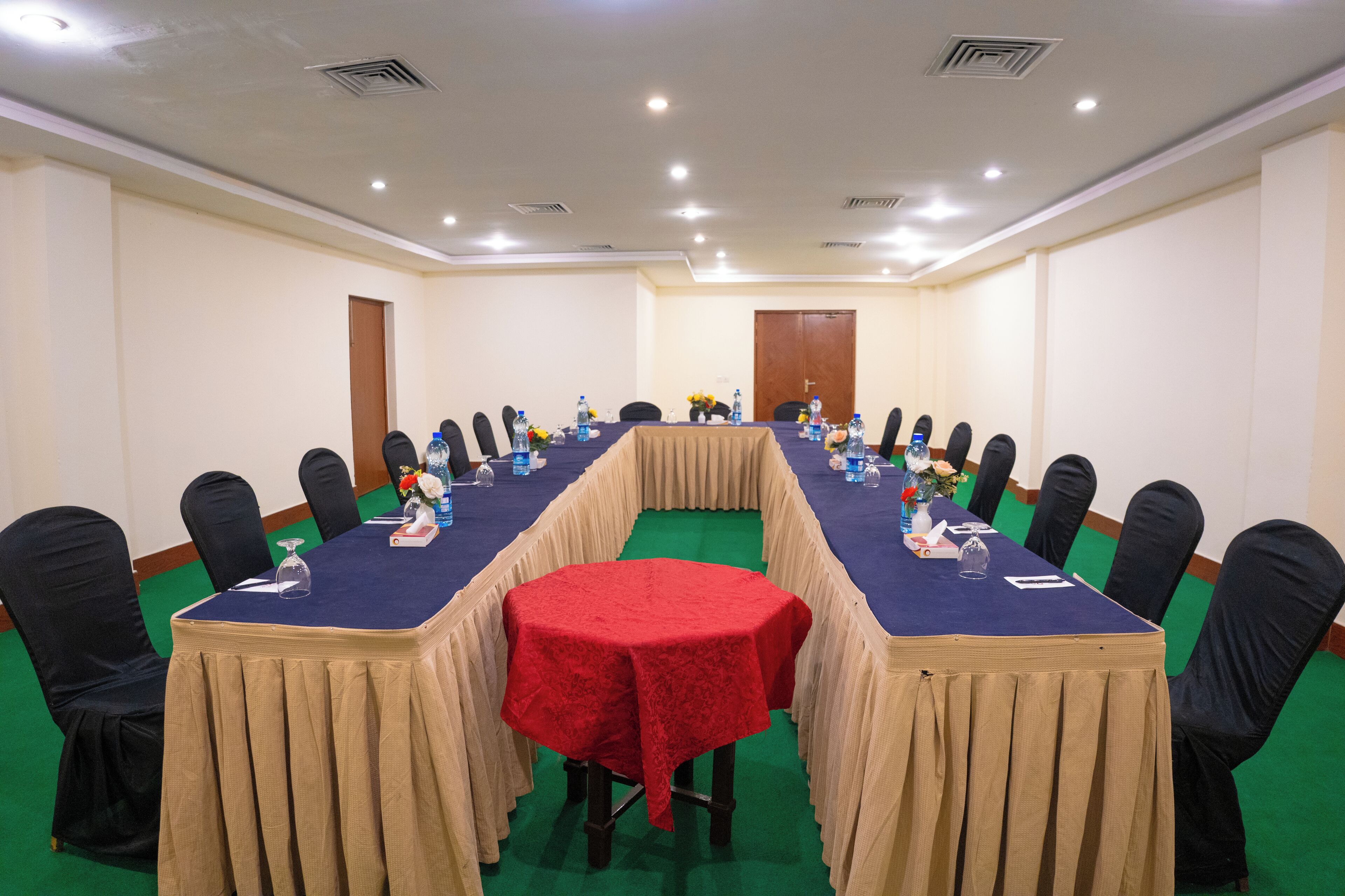 Une salle de conférence avec une longue table, des chaises noires et une nappe rouge.