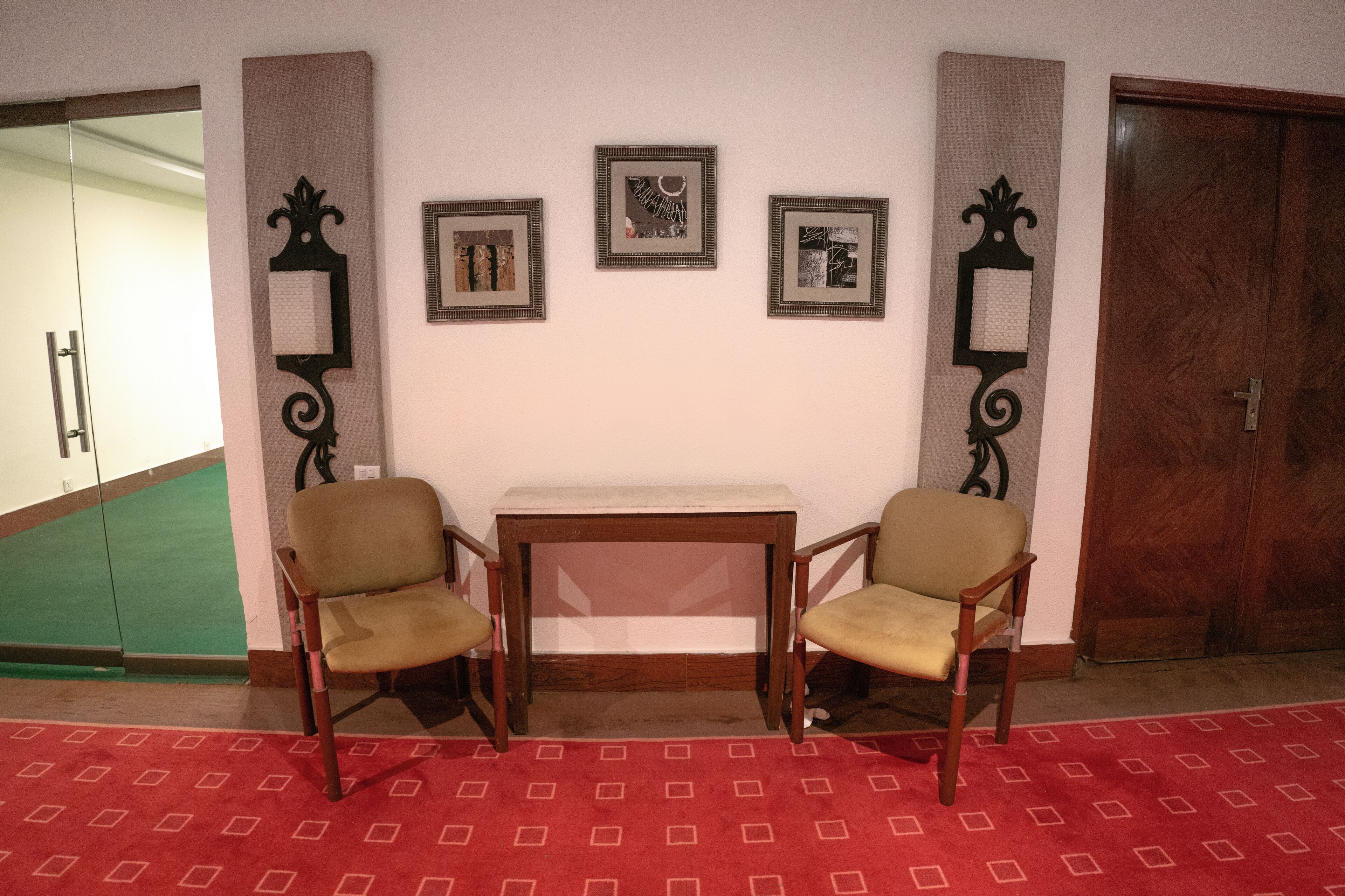 Una habitación con dos sillas de madera, una mesita y tres cuadros en la pared.