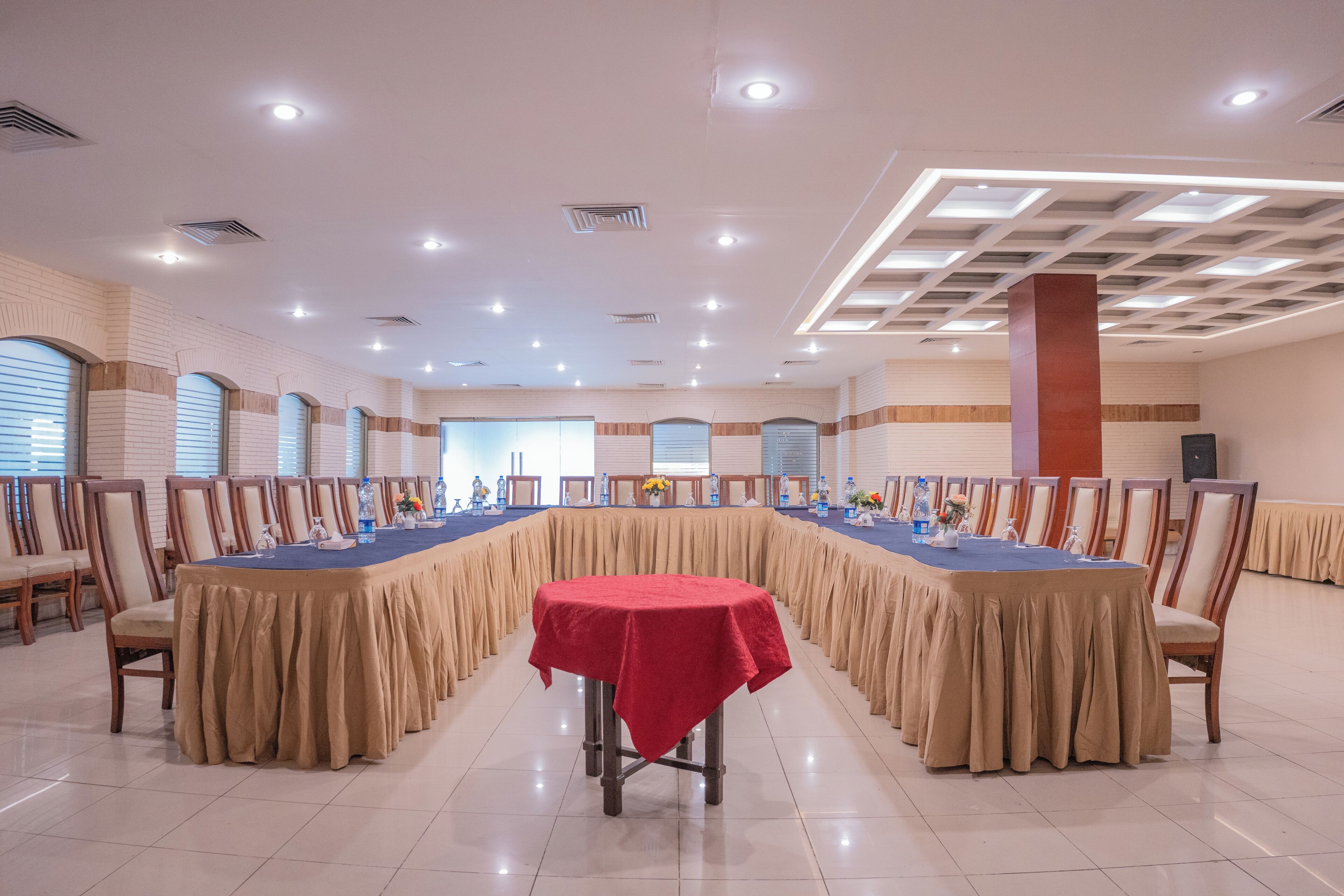 Une salle de conférence avec une longue table recouverte d’une nappe rouge, entourée de chaises.