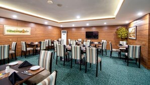Une salle de conférence équipée de plusieurs tables et chaises, d’un téléviseur à écran plat fixé au mur et d’un petit climatiseur.