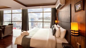Une chambre d’hôtel dotée d’un grand lit, d’un canapé, d’un bureau et offrant une vue sur la ville grâce à de grandes fenêtres.