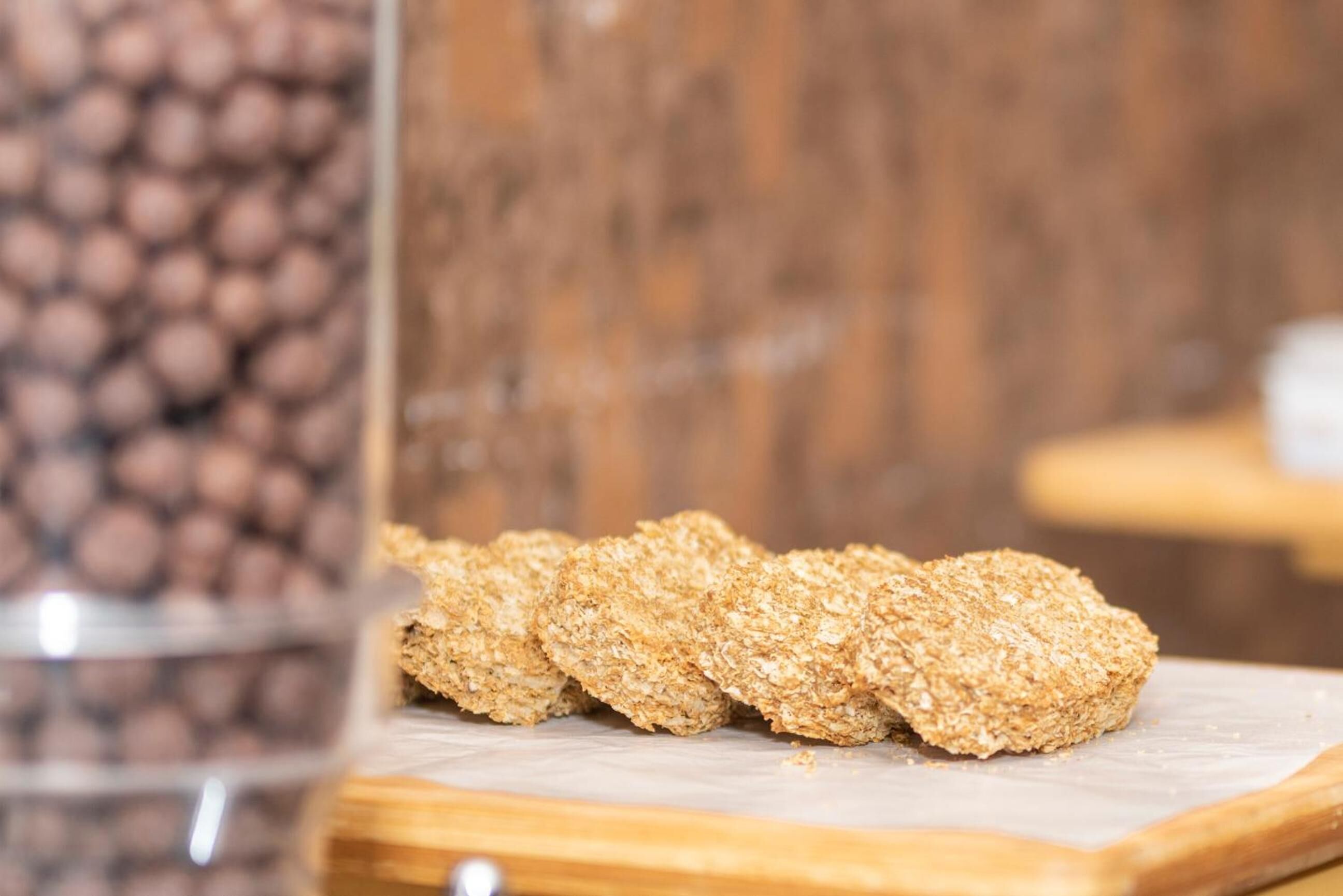 A wooden cutting board with three pieces of food coated in a crispy, golden-brown crust, possibly a type of pastry or snack, on a wooden surface.
