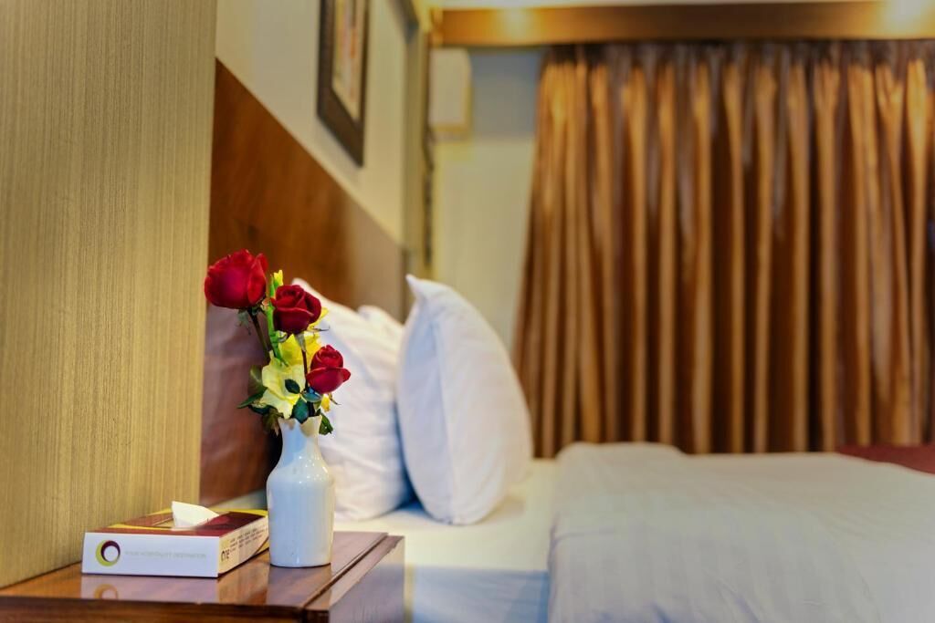 Una habitación de hotel con cama, una mesita de noche con un florero y un libro.