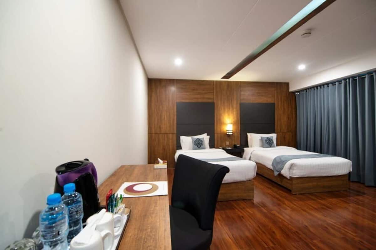 Habitación de hotel con dos camas, un escritorio de madera, una silla y una mesa con botellas de agua y una cafetera.