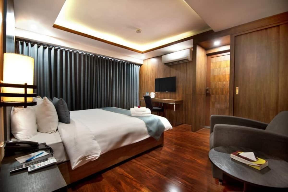 Habitación de hotel con cama, mesita de noche con lámpara, escritorio con silla, televisor montado en la pared y armario.