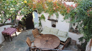 A stone patio with a round wooden table and chairs, a small round table with a checkered tablecloth, and a white wall with climbing plants. - Nazhan Hotel - Boutique Class (Selçuk)