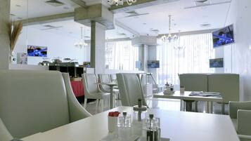 Un comedor moderno con mobiliario blanco, una araña y varias pantallas de televisión en las paredes.