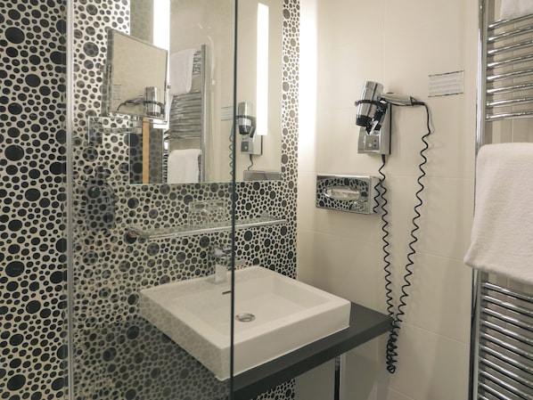Un baño con ducha de vidrio, lavamanos blanco y toallero.