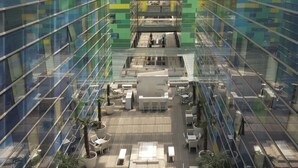 Un edificio de oficinas moderno con fachada de vidrio, varios pisos y un espacio central diáfano con asientos y mesas.