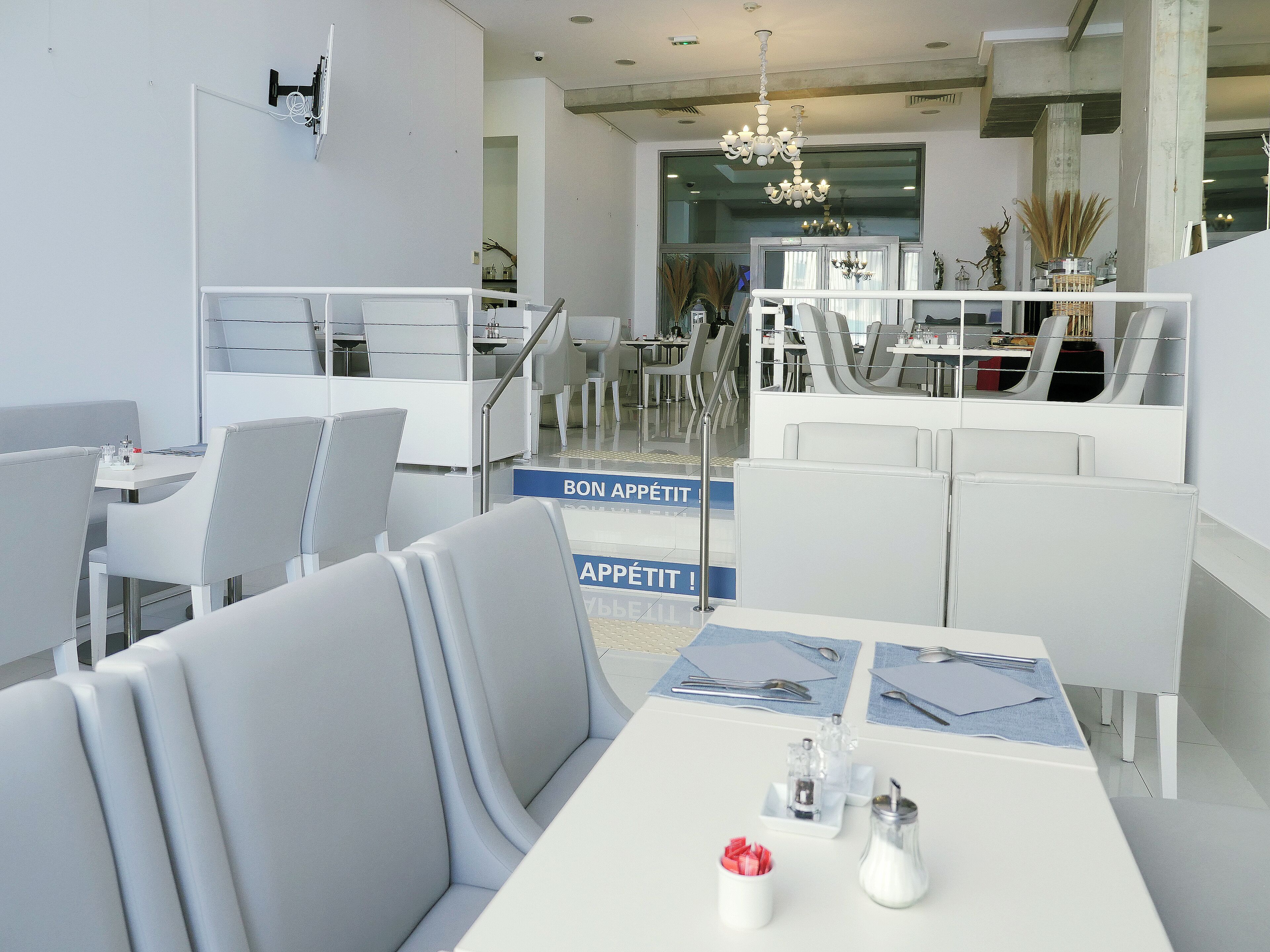 A modern dining area with white furniture, a chandelier, and a sign that reads 'BON APPETIT!'