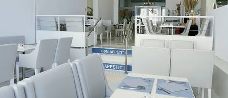 A modern dining area with white furniture, a chandelier, and a sign that reads 'BON APPETIT!'