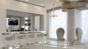 Un área de bar moderna con taburetes blancos, un espejo grande y un televisor que muestra un grupo de personas.