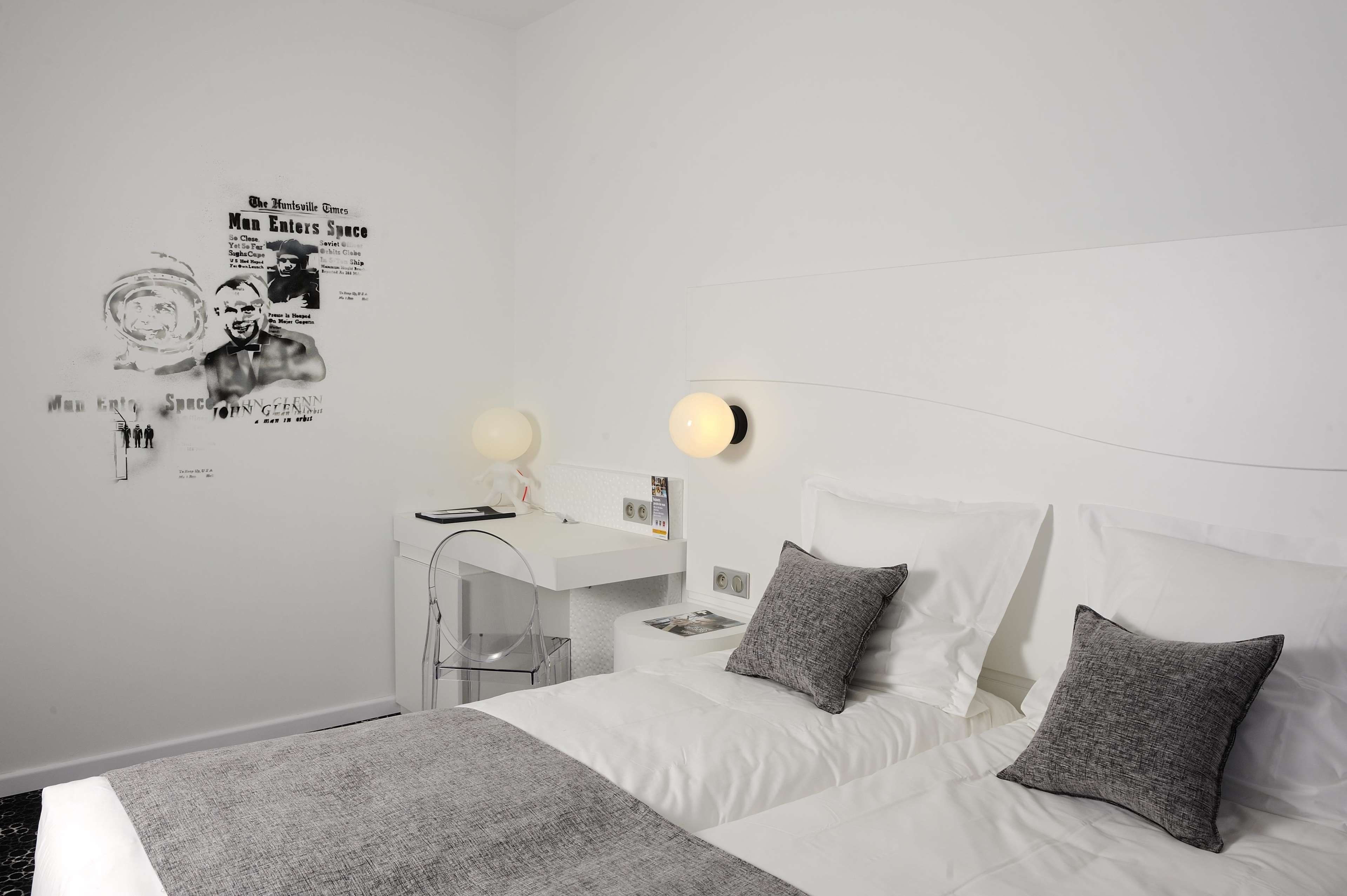 A modern bedroom with a white bed, grey pillows, a white desk, and a wall poster.