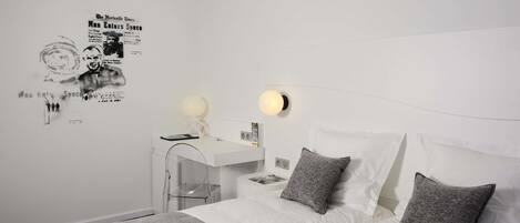 A modern bedroom with a white bed, grey pillows, a white desk, and a wall poster.